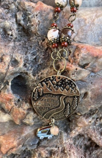 " Always Take the Scenic Route " Necklace And Earring Set Artist: Casey Hanson Zebra Jasper and brass beaded necklace with glass bead accents  Pendant reads " Always Take the Scenic Route "  Little camper trailer charm hangs below the pendant  Matching earrings with brass ear wires  20" necklace  Earrings measure 1.5" long