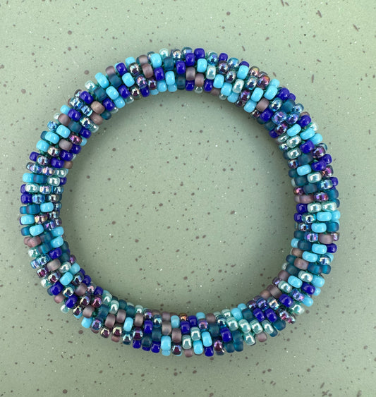 Rope Bangle Bracelet - Wave Pool Artist: Claire Pearson This Wave Pool colored beaded bangle is formed by a continuous crochets spiral and secured with a ‘mostly’ seamless join  Slightly oversized and meant to roll on and off the wrist, these bracelets are a fashionable and functional fidget piece  These tactile treats feature curated glass bead mixtures sure to dazzle and delight  One-size  Fits 7.5" wrist approximately