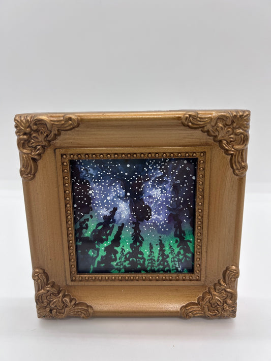 Original miniature watercolor and Ink   Grove of pine trees stand in stark shadow in front of a Wyoming star filled sky   The night sky has colors of the Aurora Borealis&nbsp;  Just envision yourself camping in the Snowy Range Mountains and looking up at this beautiful night sky  Framed in a gold colored resin frame   Easel back allows to display on a table or shelf   4" long x 4" high x .5" wide   Signed by the artist