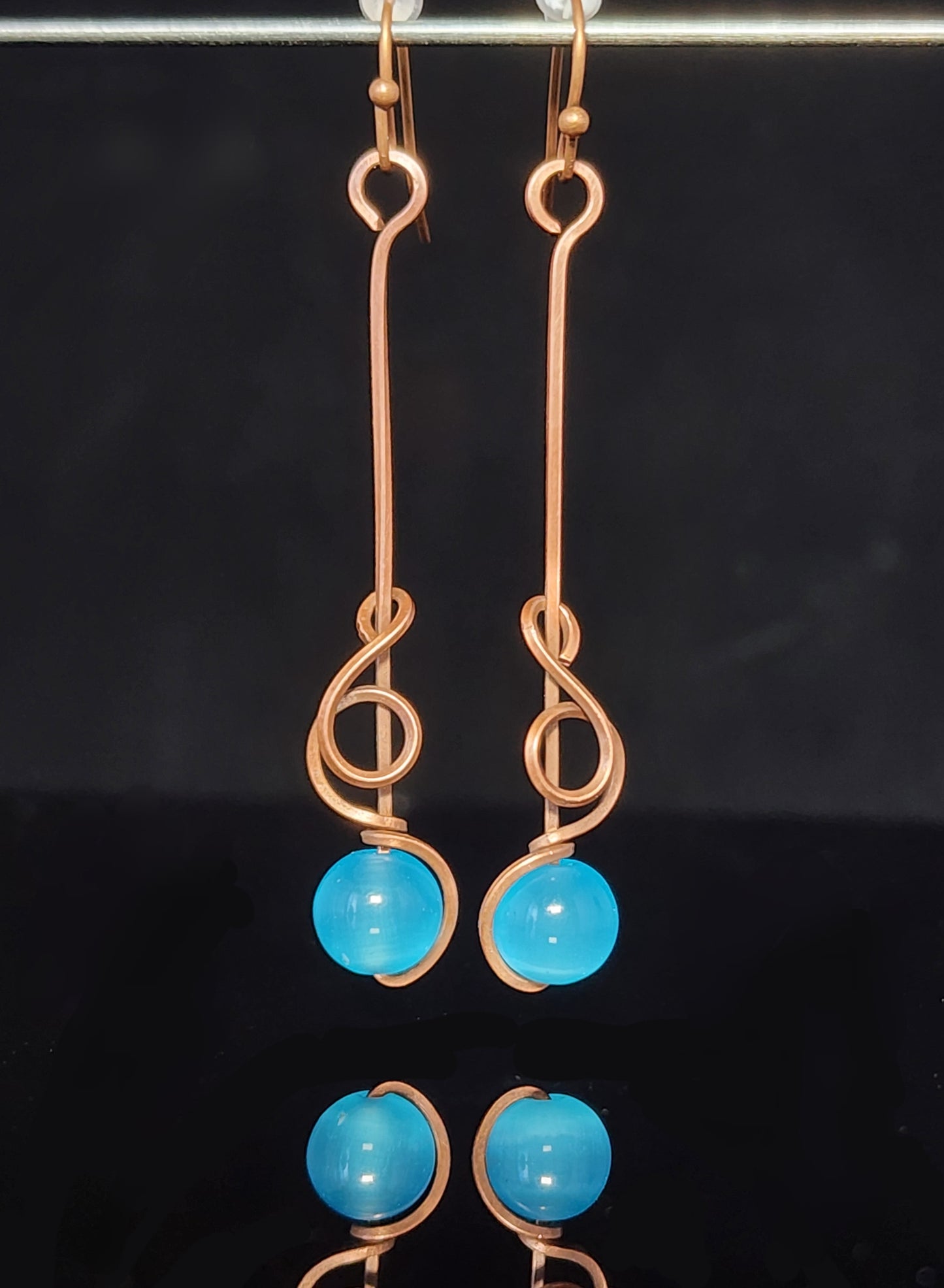 Blue Cat's Eye Sphere Dangle Earring Artist: Lindsey Griffin Brilliant Blue cat's eye sphere wrapped in copper wire 2" long x 1/4" wide Copper wires earring hooks Beautiful dangle earrings Cleaning instructions and cloth are included