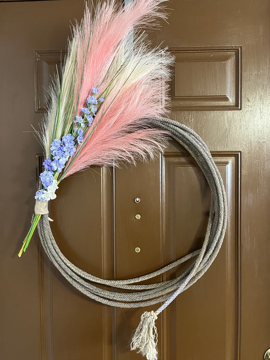 " Purple Spring " Rope Wreath Artist: Aleah Russell  Repurposed lariat rope  Rope came from an authentic Wyoming ranch  Pink and cream pampas grass with faux purple and white flowers  Bound with a burlap ribbon  Will add a touch of country to any home  34" long x 23" high x 3" wide
