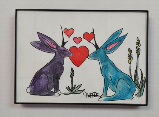 " Jackalope Love " Framed Original Watercolor and Ink Artist: Celeste Havener Original watercolor and ink drawing  A purple and a teal jackalope with hearts between them  Yellow flowers stand next to the jackalope  Framed in sleek black plastic frame  Can be hung on a wall or use the frames easel back to set on a table  Would make a great wedding or anniversary gift  7" long x 5" high x 1/2" deep