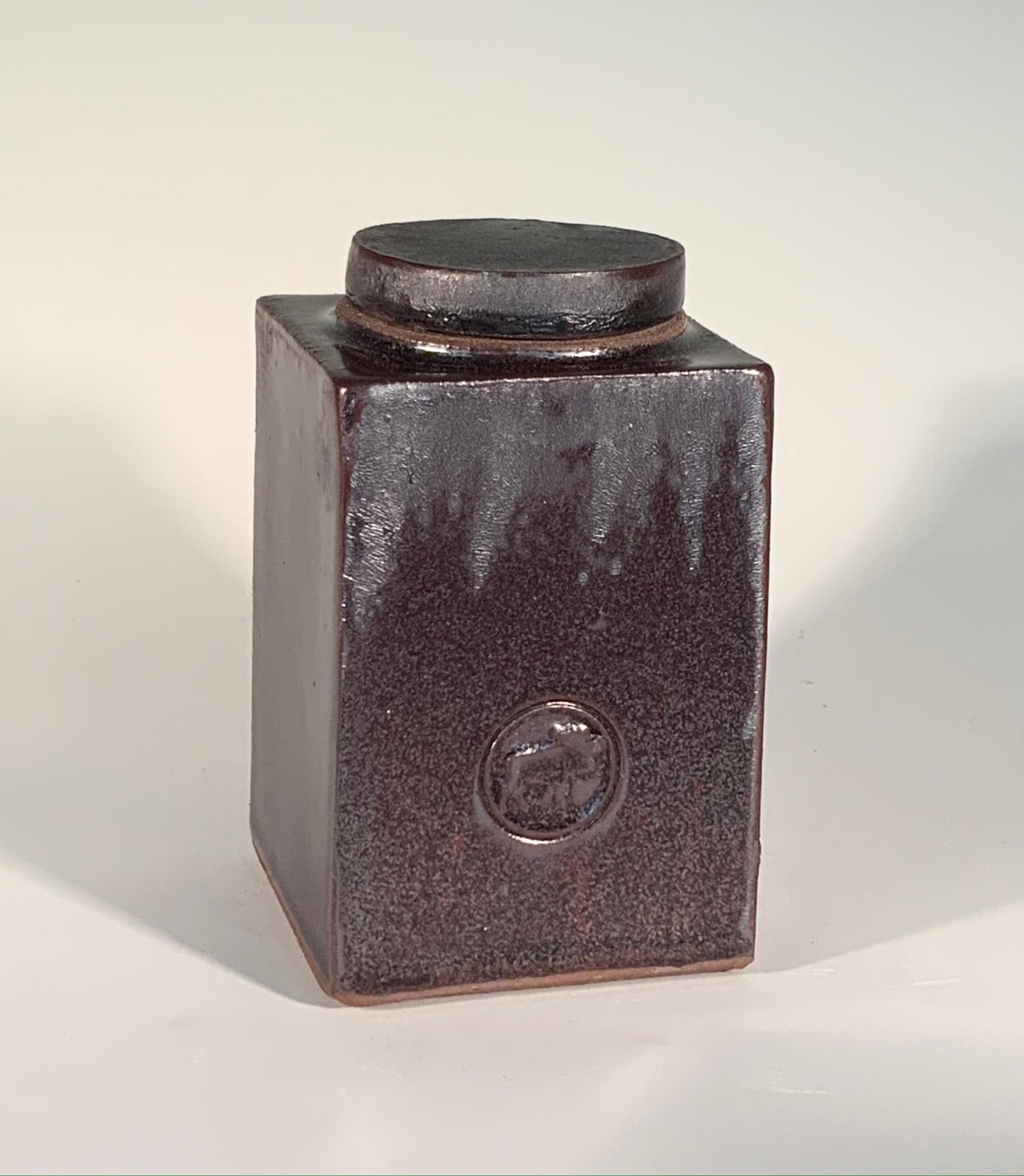 Lidded / Deep Red Moose Stamped Stoneware Jar Muffy Moore: Ceramic Potter Small dark red persimmon glaze accents lidded moose stamped on front of stoneware jar 3" Long x 3" Wide x 4.5" Deep Dishwasher safe, oven and food safe Great for dried flowers or loose tea and so on Please note Items are handmade by Artist and there is a slight variation from piece to piece