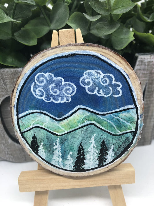Mixed media, wood slice original art <h2>"5048" Wood Slice Magnet</h2> <h2>Artist:&nbsp;Nancy Marlatt ainting of&nbsp;clouds / mountains in and around Laramie WY on wood slabs with bark edge. Picture area is 2.75" wide x 3" Long x&nbsp;.75 thick. The picture is&nbsp;mix media on a wooden slice with bark&nbsp;with magnet on back<br></p> <p>Picture would be great in a den, office or over a fire place on an easel or on your refrigerator