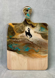 teal, brown and cream colored resin on a maple cheese board. 24K gold accents with a bucking horse and rider decal