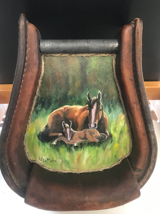 Mare and foal laying in the grass  Painted on board and framed inside of a leather stirrup  Eye-bolts and wire attached to the stirrup for hanging on a wall  One-of-a-kind piece to show your love for your Mom.