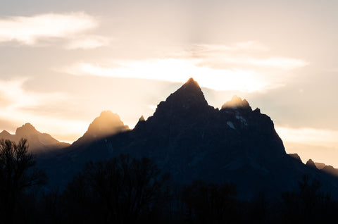 " The Finale " Grand Teton Photograph Artist: Ashleigh Monaco  Glowing light behind the Teton Range at sunset. The mountains appear black in the shadow of the sun  The Teton Mountains are in Western Wyoming, near Jackson and are a travel destination by many wanting to see the majestic mountains of Wyoming. Available in Laramie at Works of Wyoming. AVailable in lustre print and greeting card.