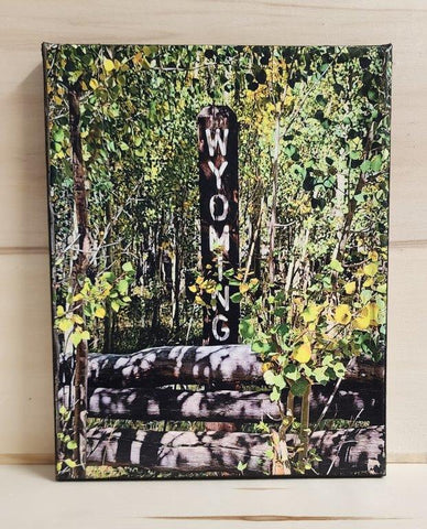 Print from a photograph  Wyoming is carved into a wooden post and painted in white  In the forest surrounded by aspen trees and behind a wooden raid fence  Photograph is printed on canvas and attached to a wooden frame  8" long x 10" high x 3/4" wide  Can be displayed on an easel, or add wire to hang