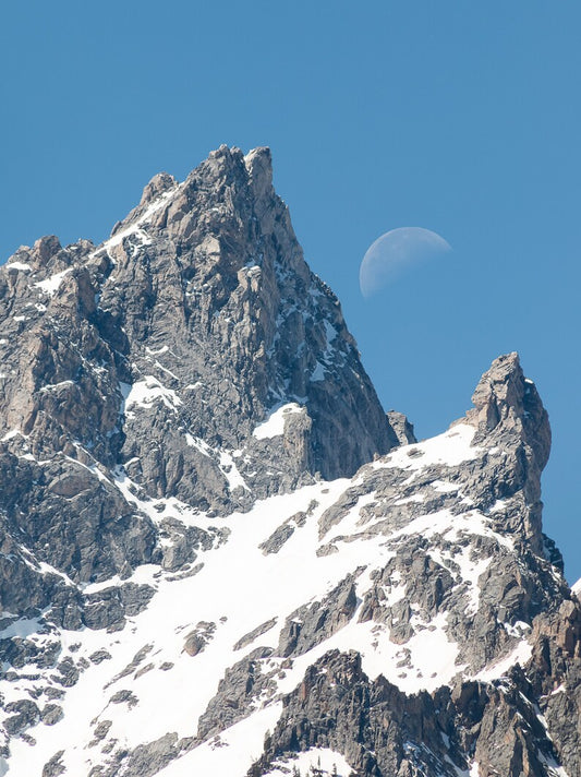 " Day Moon " Photograph Artist: Ashleigh Monaco  The Grand Teton / Teewinot up close  Snow is lingering on the rugged mountains while the moon peaks out during the day. Lustre print in protective sleeve.