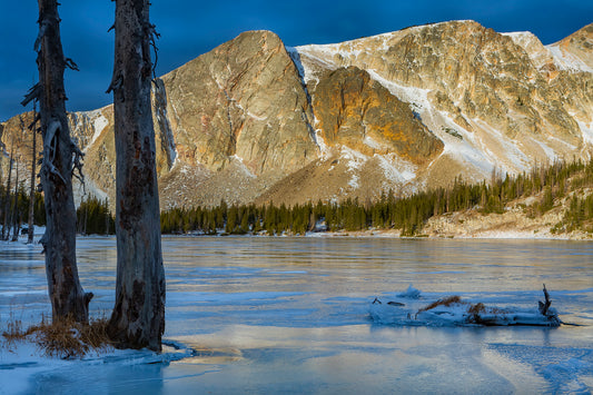 An early winter evening along the shores of Mirror Lake in the Snowy Range Mountains of Wyoming  The sun lights up Medicine Bow Peak of the Snowy Range in the background  Ice covers the lake in front of the mountain