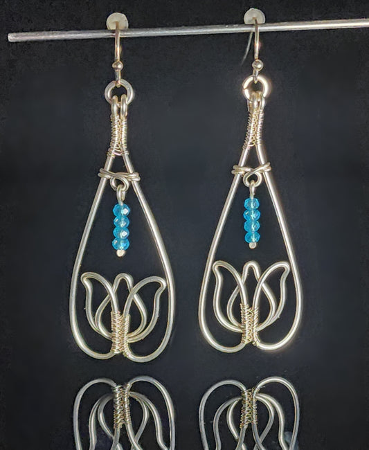 Blue Bead Silver Tulip Earrings Artist: Lindsey Griffin Hand worked colored artistic wire  Teardrop with Tulip shape at the bottom  High end blue beads hang above the tulip flower  Copper ear wires  2.16" long x .84" wide