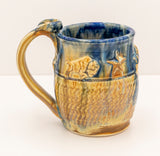 Hand Thrown Stoneware Pottery  Handled Mug  Textured Bison and Star along the sides of the mug  Blue glaze around the lip of the mug and drips down the side  3" wide x 4.25" tall  Approximately 16 oz mug  Food safe  Lead Free  Top rack safe, but handwashing is best
