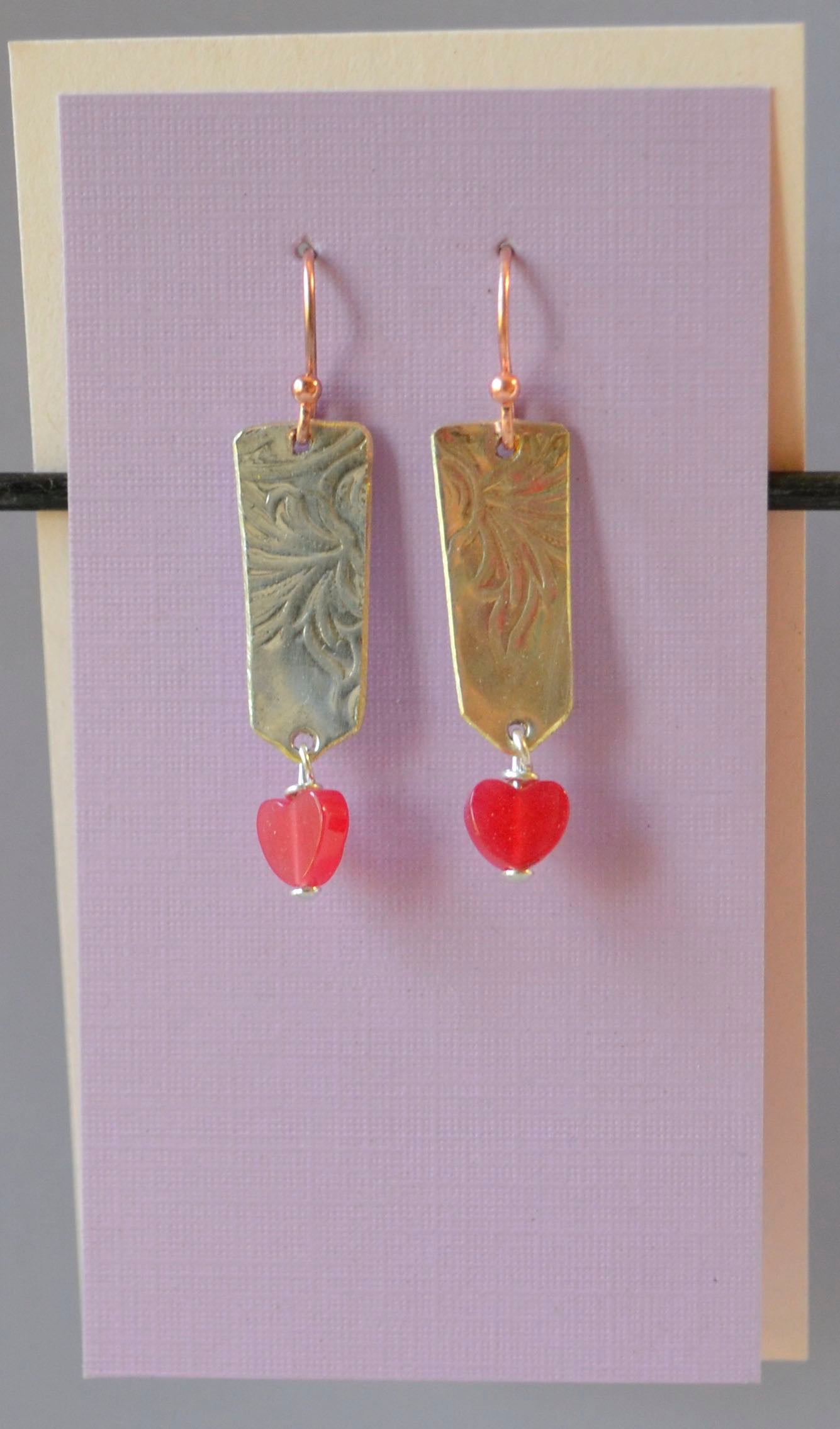 Red dyed jade hearts hang below embossed recycled silver plate  1/4" wide x 1 1/2" high  Rose gold ear wires