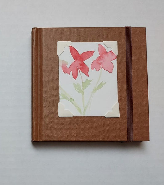 Brown colored mini sketchbook  Brown stretch band helps hold the book closed  Original watercolor of Poppy flowers attached to the cover  Blank pages inside  A great little sketchbook to take with you  Keep in a pocket or bag and take with you when you go  4" x 4" x 3/4"