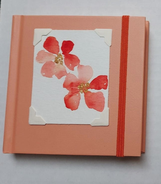 Peach colored mini sketchbook  Orange stretch band helps hold the book closed  Original watercolor of Habiscus Flowers attached to the cover  Blank pages inside  A great little sketchbook to take with you  Keep in a pocket or bag and take with you when you go  4" x 4" x 3/4"