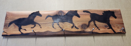 Wood Burned Horses With Horseshoe Nails Hanger Artist" Michael McMahon  Silhouettes of running horses wood burned into a cedar wood backer  Clear coat finished  3 horseshoe nails hammered into bottom of wood block can be used for hanging keys  24" long x 5.5" high x 2" wide  Two Sawtooth hangers on the back for wall mount  Wire has also been added for hanging the piece, however the sawtooth will be more secure and balanced when hanging in your home