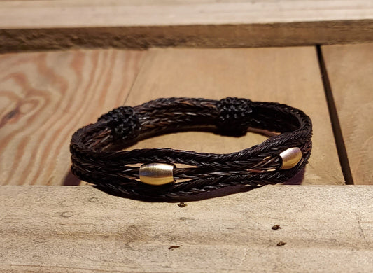dark colored hand braided horsehair bracelet with two brass beads. bracelet has adjustable knots also from horsehair