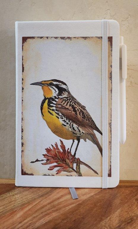 " Meadowlark and Paintbrush" White Journal with Pen.  Artist: Catherine Holt  White leather covered journal  On the cover of the journal Wyoming's State bird, the Meadowlark, is standing on Wyoming's State flower, the Indian Paintbrush   Cover art is from an original painting by the artist  Lined pages with ribbon to mark your page  Pen and elastic pen loop included  Elastic band helps hold journal secure  4.5" long x 5.5" high  A beautiful journal for everyday writing, Art Journaling and note keeping.