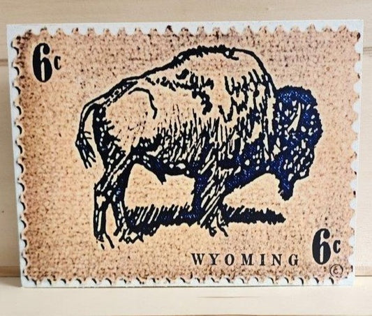 " 6 Cent Stamp " Wyoming Bison Wood Print Artist: Catherine Holt Wooden print from the artist's design  Vintage looking 6 cent stamp with a bison in the center and Wyoming in lower right  8" long x 6" high x 3/4" wide  On a wooden frame  Eye bolt and string attached to back to hang the piece, or could also be displayed with an easel (not included)