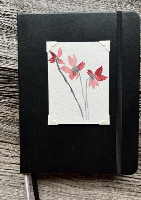 Hardcover black lined journal  Black elastic band helps hold the book closed  Ribbon page marker  Original watercolor of 3 Red flowers attached to the cover  Lined pages inside  A beautiful journal for young and old alike  6" long x 8" high x 3/4" wide