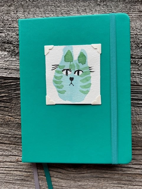 Hardcover teal cover journal with dot / bullet pages  Teal elastic band helps hold the book closed  Ribbon page marker  Original watercolor of a blue and green Kitty Cat attached to the cover  Dot / bullet pages inside  A beautiful journal for young and old alike  6" long x 8" high x 3/4" wide