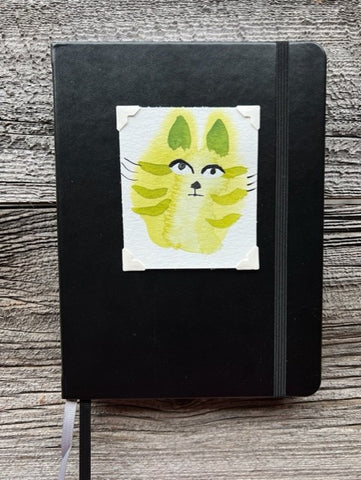 Hardcover black lined journal  Black elastic band helps hold the book closed  Ribbon page marker  Original watercolor of a green Kitty Cat attached to the cover  Lined pages inside  A beautiful journal for young and old alike  6" long x 8" high x 3/4" wide
