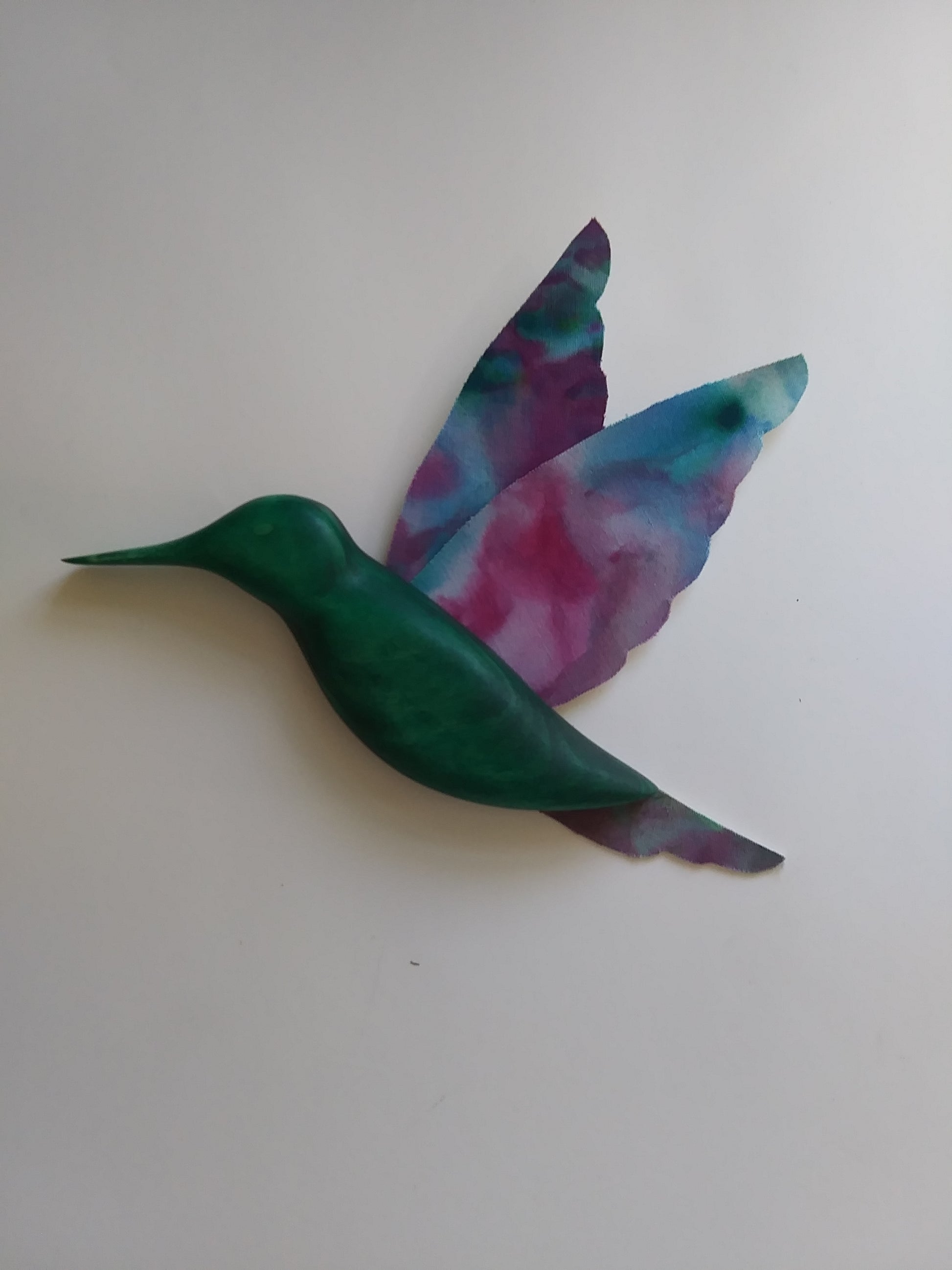 "Humming Bird" Green Tye Dye Bird Stained Glass Artist: Bruce Allemani  Green wood body with Tye dye wings and tail of the humming bird  8" long x  5" wide x  1"  Would look great hanging in a living room or a window  Please note, each piece is custom designed by the Artist , with a slight variation between each piece