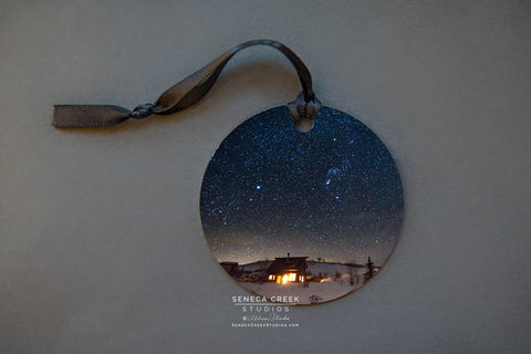 Starry Cabin Metal Print Ornament Photographer: Allison Pluda, Seneca Creek Studios  A hanging photograph metal ornament    A photographic picture of a starry cabin up in the  Snowy Range mountains     Picture on both sides of the ornament and the ornament hangs with a ribbon  Please note, each photograph for the ornament has been taken by the Artist 