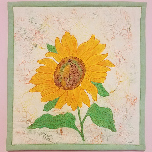 Sunflower Fiber Art Wall Hanging Artist: Crystal Lawrence 17" wide x 18" Fiber Wall Hanging  One Sunflower  Hand stitched Batik background  Wooden dowel inside fabric loops on the back of piece for hanging
