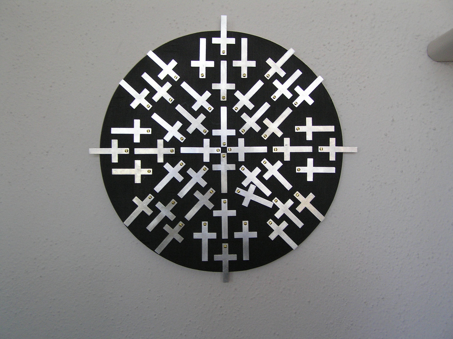 "Cross Roads" Mandalas w / Cross Mixed Media Artist: Bruce Allemani Round black board with aluminum crosses   Brass screws hold crosses on round black board  Wire on back for wall hanging  12" long x 12" wide x 1/2" high  Please note, each piece is custom designed by the Artist , with a slight variation between each piece