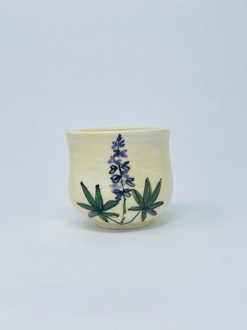 Hand thrown porcelain  Wide bellied juice or wine cup  Purple Lupine motif is hand painted on the side of the cup  A yellow wash gives added color to the porcelain  Glazed porcelain allows for everyday use  3.5" long x 3.5" wide x 3" high  It is suggested to hand wash the cup