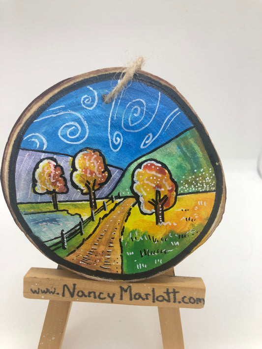 " Follow The Fence Line " Original Wood Slice Ornament. Country road following a fenceline going to the mountains with breezy swirling clouds in the sky