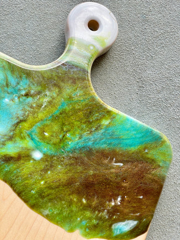 Artisan Cheese Board / Handle Artist: Marcy Knotwell  Aqua blue, green, and brown resin design  You will not be disappointed with the quality of this product! Our handcrafted wood grained-edge charcuterie cheese boards are the answer to stylish, multi-functional, sustainable serve-ware.  When not in use, this charcuterie cheese board makes a beautiful addition to your countertop or gallery wall.