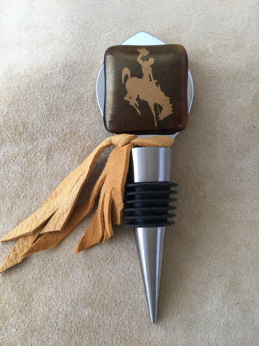Fused glass  accent with 22 kt gold foil of bucking horse, Steamboat, UWYO's logo, onto a stainless steel bottle stopper, accented with fringed buckskin