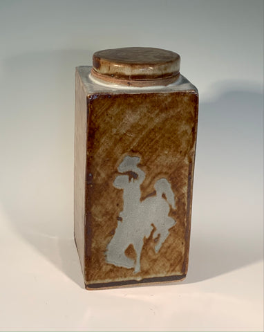 large rectangle jar in tan and white glaze. University of Wyoming logo "Steamboat" is prominent on one side of the jar. Round stoneware lid