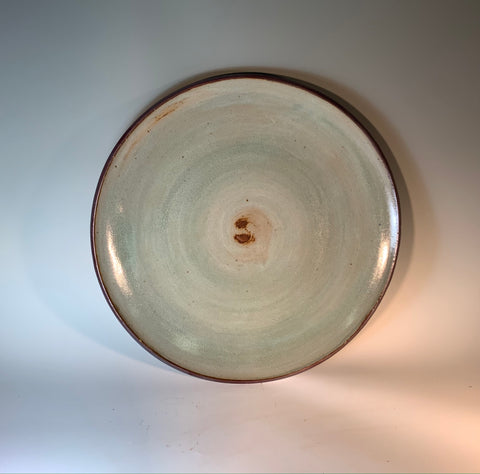 large round stoneware platter. pale green glaze with iron accents