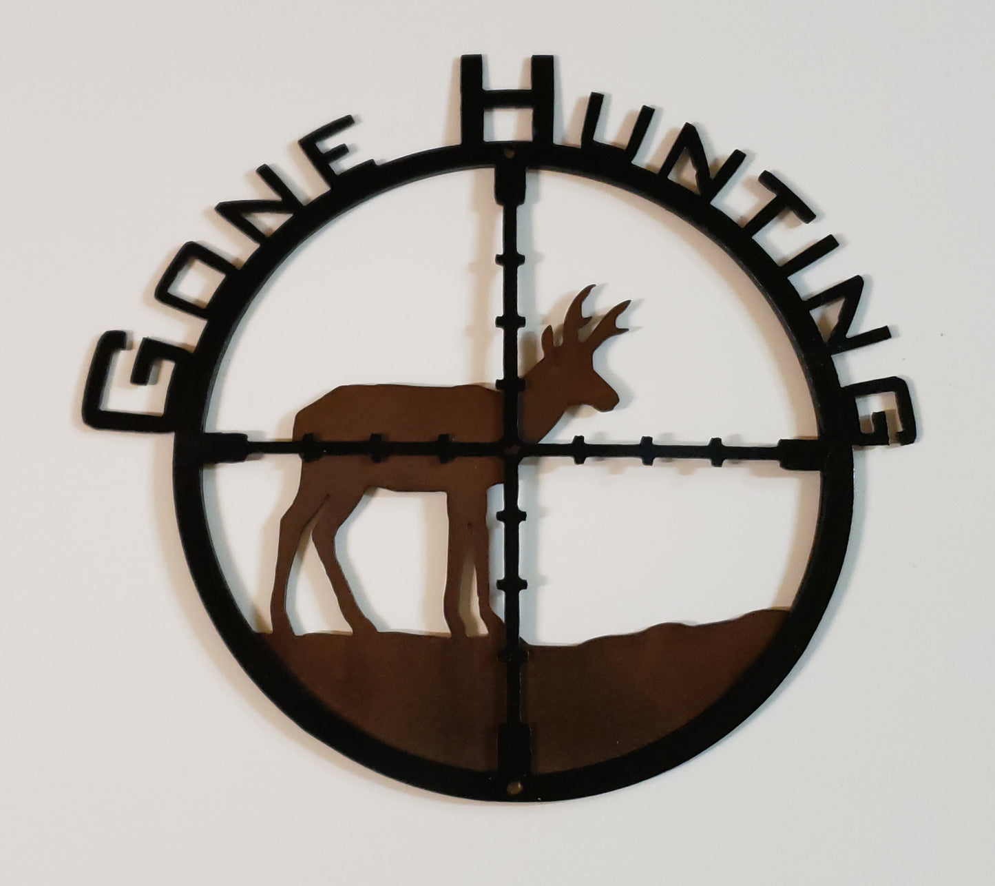 A medium metal sign with gone hunting cut out in it and a pronghorn in the cross hairs of a gun sight  Grinded and sandblasted with polished heat finish rustic patina colors  Glossy clear coat protective enamel  13" long x 12" wide x 1" high  Perfect for that man cave or rustic cabin 