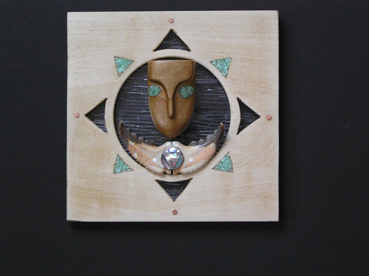 small wooden face with inlayed stone eyes. claw and metal embellishment. wooden bacground with cutout for glass