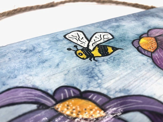 Original  watercolor painting with acrylic pen on a wood panel by Laramie, Wyoming Artist, Nancy Marlatt.  Fun, cheerful, spring,  purple flowers dance across the panel while  a bumble bee flies above them