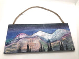Original watercolor mixed media by Wyoming Artist, Nancy Marlatt of Laramie. Enjoy this original watercolor. mixed media painting with acrylic pen on a wood panel . It measures 12" x 5.5" x .25 ". A Jute string hanger is provided.Find the hidden wildlife animals in the mountain range