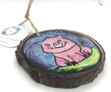 " Piggie" Hand Painted Wooden Ornament Artist: Nancy Marlatt  Original watercolor painting on a small slice of wood  Hand painted natural wood slice with a jute string attached  May be displayed as miniature artwork or as a holiday tree ornament