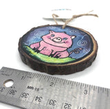 " Piggie" Hand Painted Wooden Ornament Artist: Nancy Marlatt  Original watercolor painting on a small slice of wood  Hand painted natural wood slice with a jute string attached.  A decoupage typographical map was adhered to the wood slice before painting  Surface was treated with a transparent watercolor ground  Actual size and Hand signed by the artist  3" x 3" .25" 