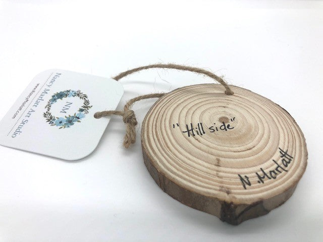 " Hill Side " Hand Painted Wooden Ornament Artist: Nancy Marlatt  Hand painted natural wood slice with a jute string attached  Original watercolor painting  Actual size and weight varies per piece  Hand signed by the artist