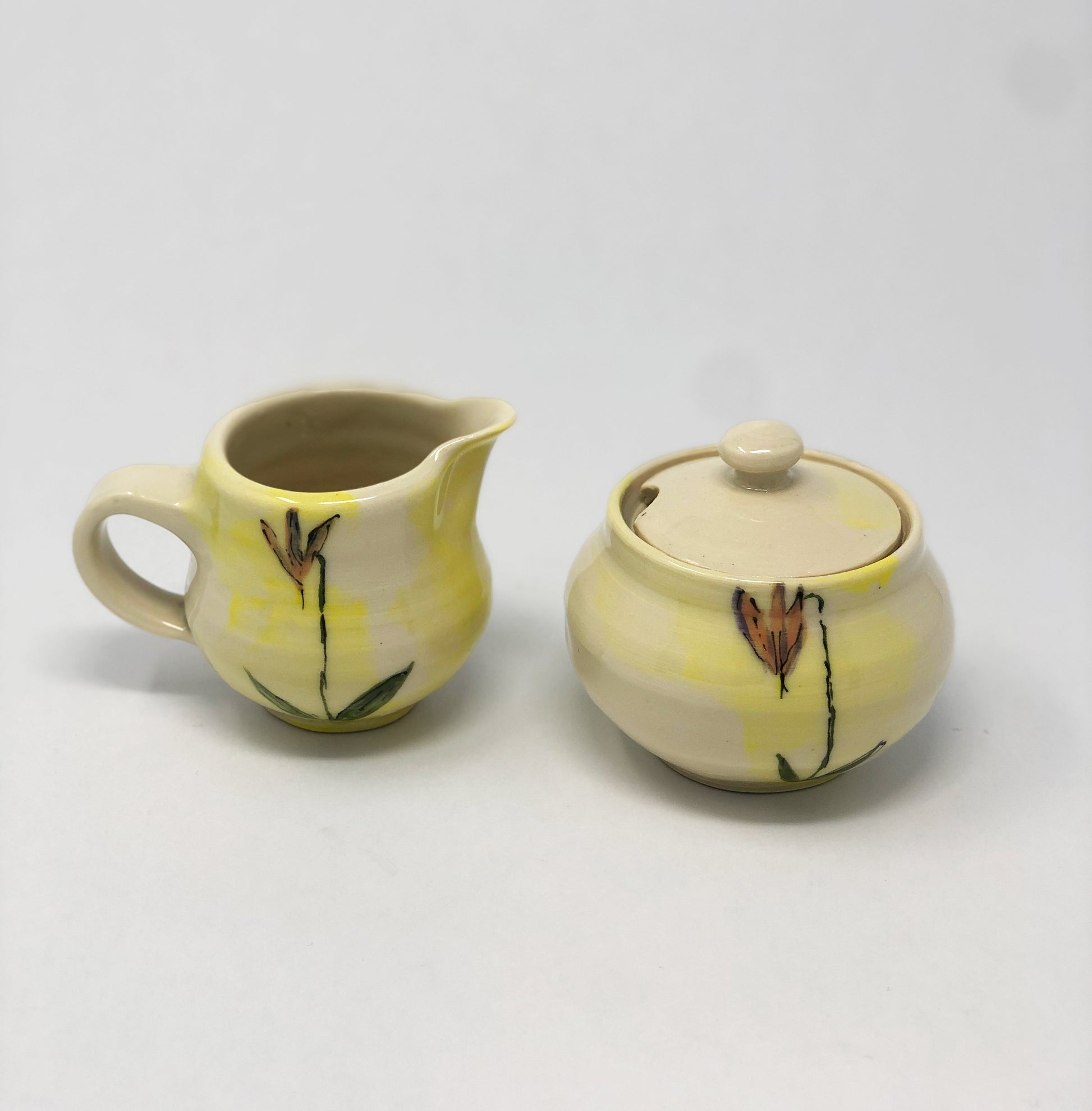 Sugar bowl and creamer set. Hand thrown porcelain with yellow wash. Wyoming native flower Shooting Star hand painted on the sides. Spoon slot in sugar bowl lid.