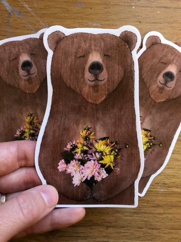 Big Bear With Bouquet Vinyl Sticker Artist:  Tara Pappas  Brown bear holding a bouquet of flowers  Easy to stick on  3" wide x 5" high  Would look great on a water bottle or computer
