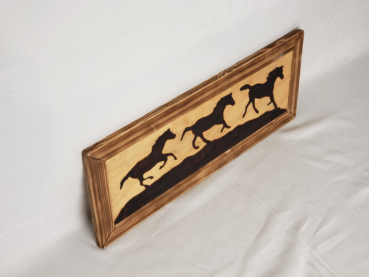 Wood Burned Horses In Wooden Frame Artist" Michael McMahon  Silhouette of three horses running on a hill  Burned into plywood with wood burned frame  Coated in clear polyurethane finish  Metal wire hanger on the back  28" long x 12" high x 3/4" wide  Would be a great gift for any cowboy or cowgirl