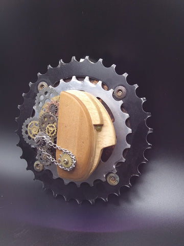 Wooden head form with jade bead eye and small gears attached to the back of the head  All attached to metal bike gears and a wooden back  Wire attached to the back for hanging  5" long x 5" wide x 2.5" high