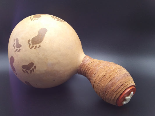 Gourd Rattle with bear paw tracks hand painted around the side of the gourd  Leather wrapped around the stem of the gourd as a handle  White bone bear attached to the base of the stem  Functional artwork or use as decoration  Not intended as a child's toy