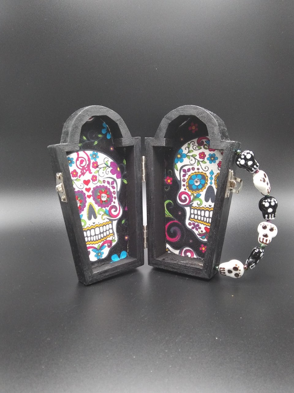 Wooden coffin with a wooden cross attached to the front  Glass skull bead handle  Metal clasp and hinges  Day of the Dead cloth interior