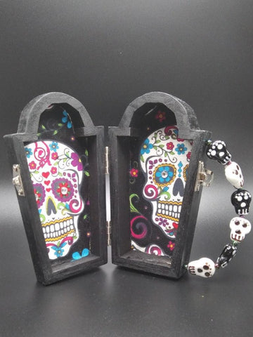 Wooden coffin with a wooden cross attached to the front  Glass skull bead handle  Metal clasp and hinges  Day of the Dead cloth interior